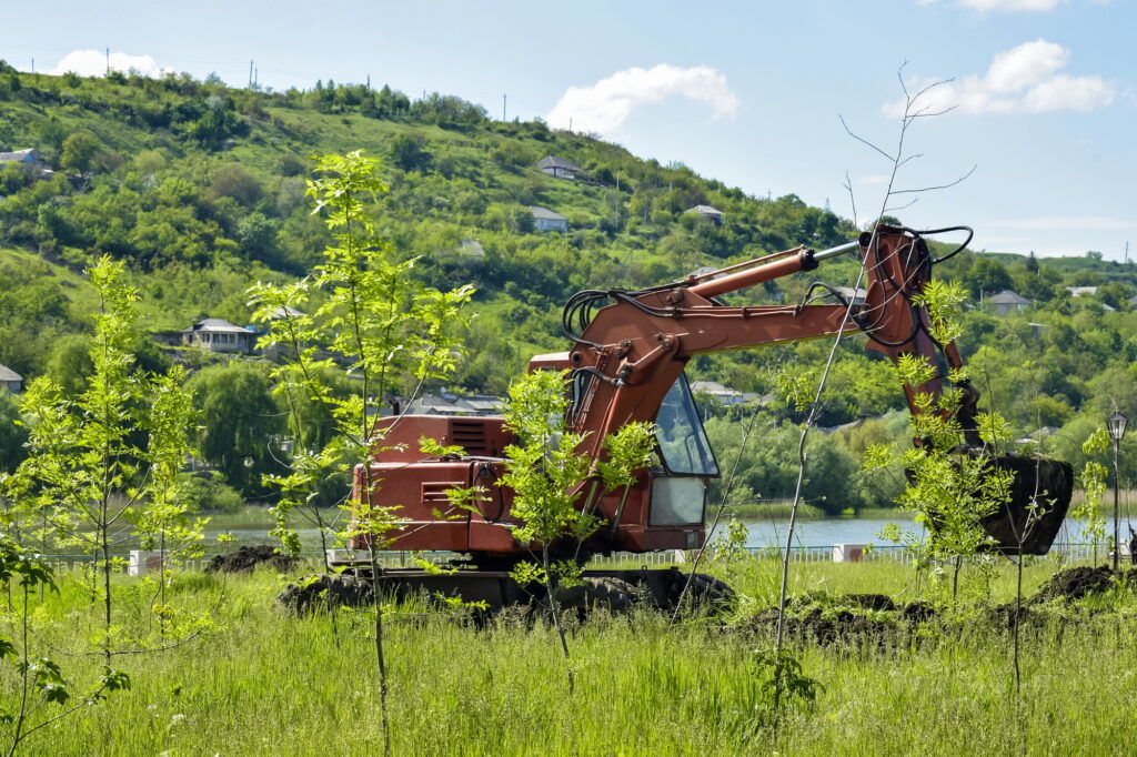 Construction machinery at Work. Red excavator digs into the earth on a lush green hillside